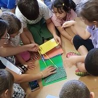 Children, sitting on the floor in a circle, building a book with pages enriched with NFC tags that activate snippets of a story told by them on a smartphone.