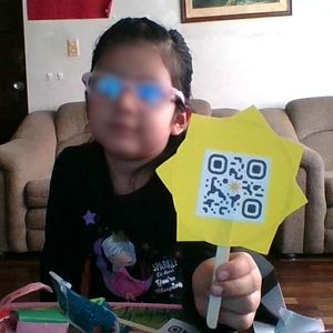 Una niña participante del piloto mostrando un sol de papel con código QR mientras toma una foto interactuando con el sistema "Aquarela Virtual".