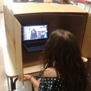 Criança imitando uma expressão emocional na "caixa telepática" na frente do computador.