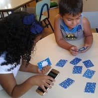 Dos niños jugando un juego de memoria en el que las tarjetas son todas iguales y su contenido se revela mediante audio al tocar la tarjeta con un teléfono inteligente equipado con NFC.