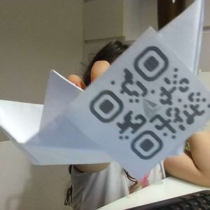 Niño mostrando un barco de papel con código QR mientras toma una foto interactuando con el sistema "Aquarela Virtual".