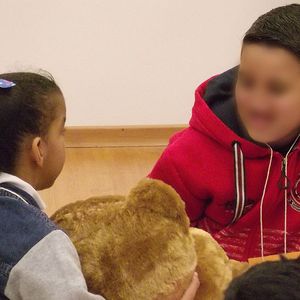 Crianças sentadas no chão abraçando e passando o urso Teddy de mão em mão