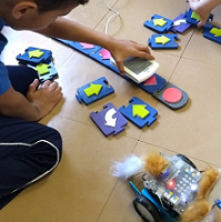 Cuatro niños observan el movimiento del robot mBot que está ejecutando el programa tangible que crearon los niños usando los bloques de madera de TaPrEC.