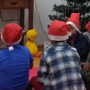 Children sitting on the floor in a circle looking at the screen.