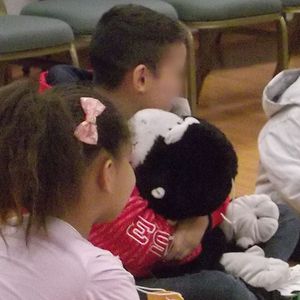 Niños sentados en el suelo abrazando y pasando de mano en mano a Chico, un mono de peluche con tecnología integrada para detectar abrazos.