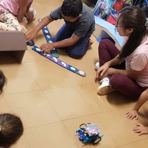 Duas crianças estão criando um programa tangível para o robô MBOT entrar em uma garagem de papelão. A classe está observando e aplaudindo seus amigos.