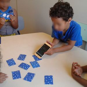 Um garoto está lendo uma etiqueta NFC usando um smartphone, outro garoto está contando as cartas que ganhou e algumas meninas estão esperando a sua vez de jogar.