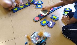 Criança manipulando um leitor RFID sobre peças de madeira para programar os movimentos de um carrinho robô.